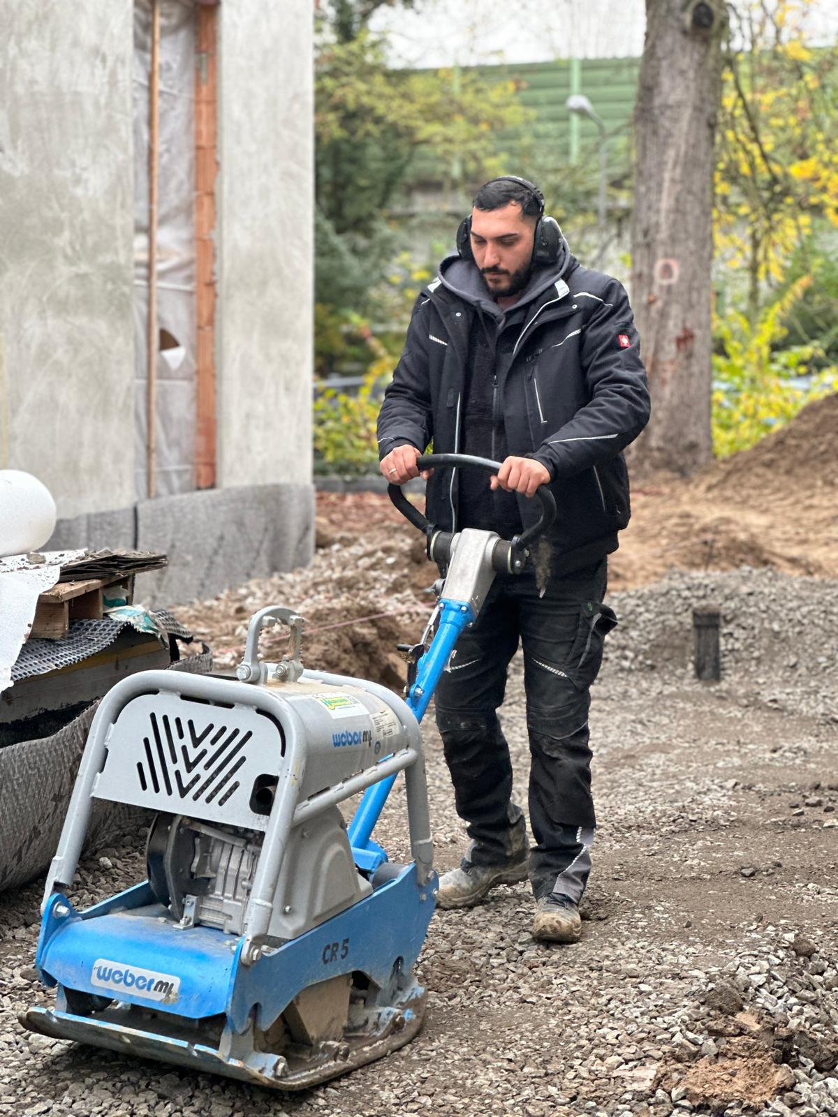 Mitarbeiter von Eymen Galabau verdichtet mit einer Rüttelplatte den Untergrund einer Baustelle