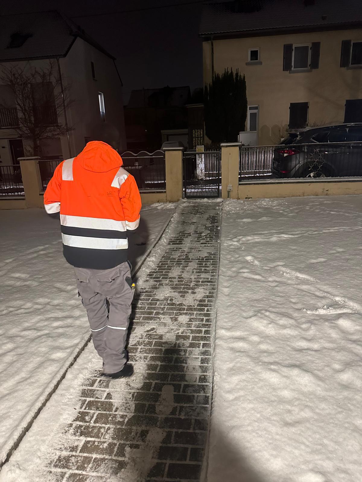 Geräumter und gestreuter Gehweg im Schnee bei Nacht während des Winterdienstes